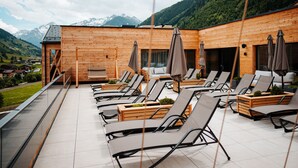 Un bâtiment en bois doté d’une terrasse avec des chaises longues et des parasols, offrant une vue sur un paysage montagneux.