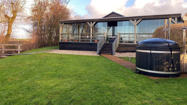 A modern house with a large glass window, a wooden deck, and a barbecue grill. - Cottage in Paesens Near Wadden Sea (Paesens)