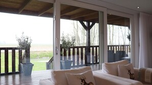 An open sliding door leading to a deck with a view of a grassy field and trees. - Cottage in Paesens Near Wadden Sea (Paesens)
