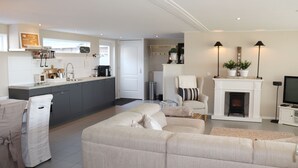 A modern kitchen with grey cabinets, a dining area with a covered table, a living room with a sofa and a fireplace, and a television on a stand. - Cottage in Paesens Near Wadden Sea (Paesens)