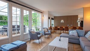 A modern living room with a sofa, armchairs, a coffee table, and a dining area with chairs and a table. Large windows provide natural light and a view of the outdoors. - Holiday Home in VÃ¦ggerlÃ¸se (Vaeggerlose)