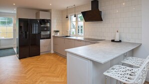 A modern kitchen with a built-in oven, a large island with bar stools, and a window providing natural light. - Holiday Home in VÃ¦ggerlÃ¸se (Vaeggerlose)