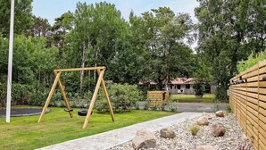 A wooden swing set in a landscaped garden with a paved path, rocks, and a fence. - Holiday Home in VÃ¦ggerlÃ¸se (Vaeggerlose)