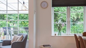 A room with a large window, a chair, a small table, and a clock on the wall. - Holiday Home in VÃ¦ggerlÃ¸se (Vaeggerlose)