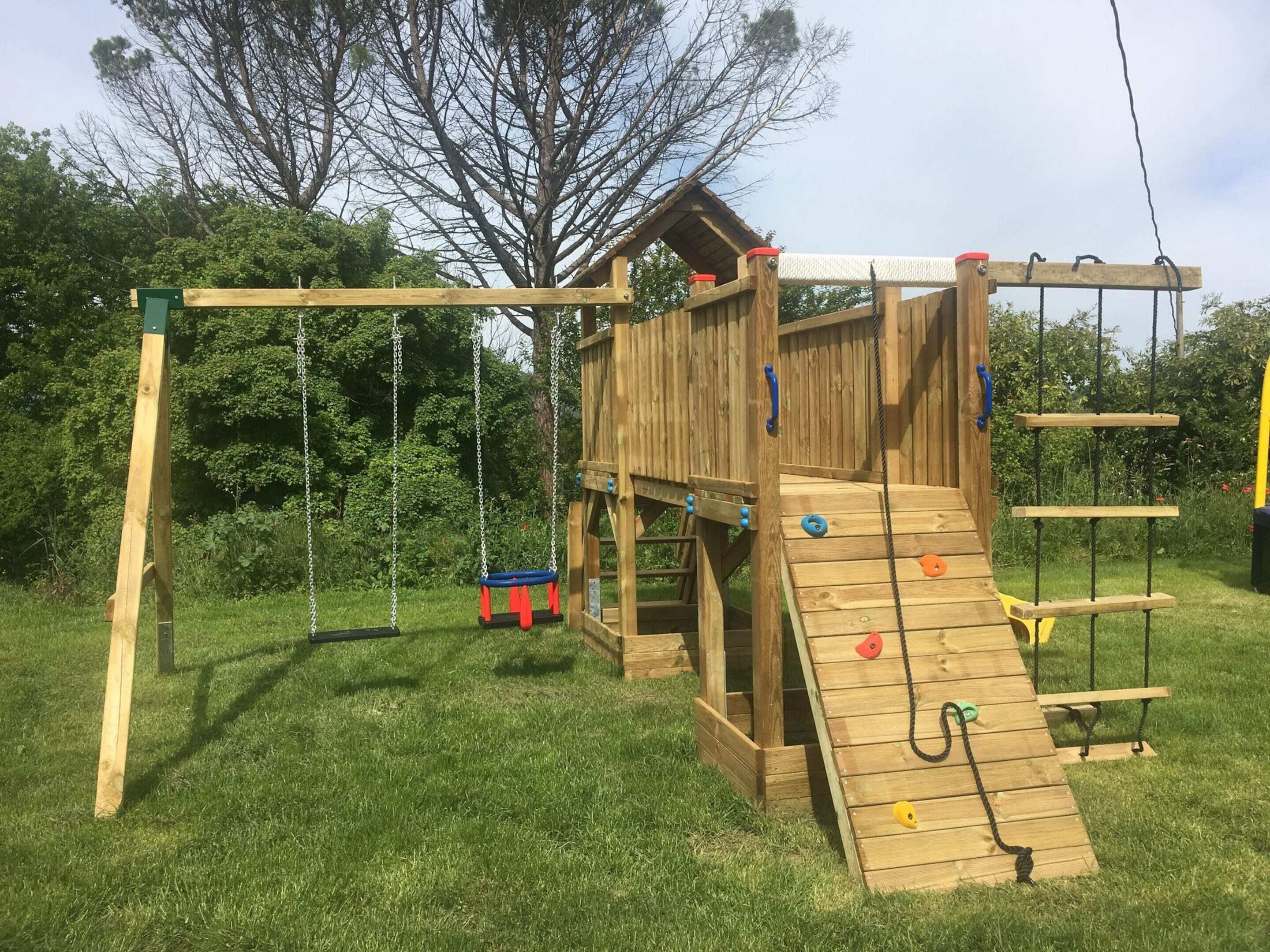 Une structure de jeu en bois comprenant une balançoire, un filet d’escalade et un toboggan.
