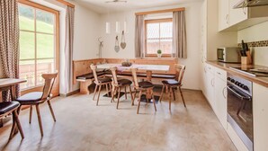 A kitchen with a dining area, wooden furniture, a built-in oven, and large windows with curtains. - Apartment in Hainzenberg Near Ski Lift (Hainzenberg)