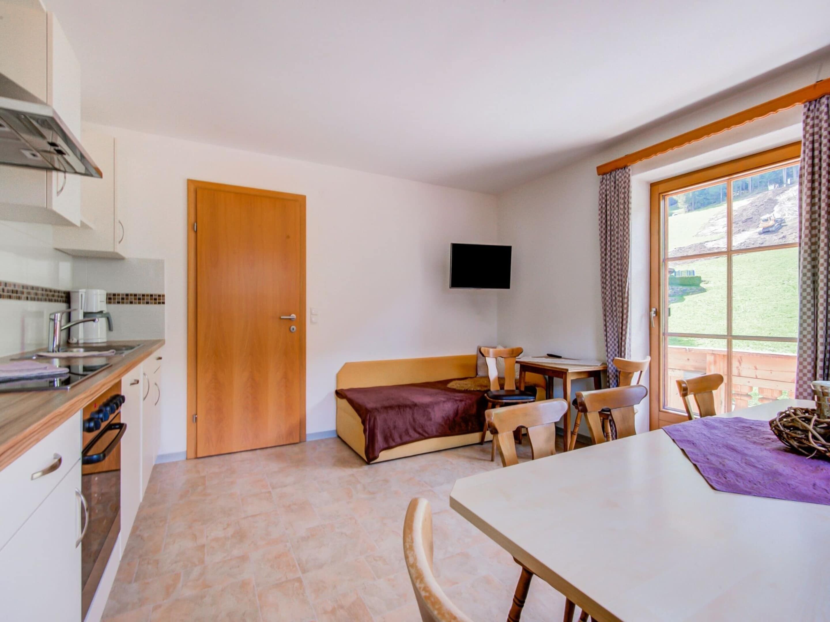 A compact room with a kitchenette, a sofa, a dining table, and a TV.