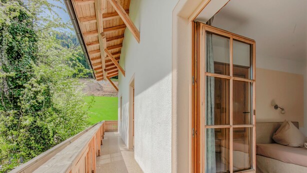 A balcony with a wooden railing, a sliding glass door, and a view of greenery. - Apartment in Hainzenberg Near Ski Lift (Hainzenberg)