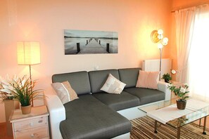 A living room with a sofa, a glass coffee table, a lamp, a plant, and a painting on the wall.