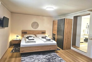 Ein modernes Schlafzimmer mit Bett, Nachttischen, einem Fernseher und einem großen Spiegel.