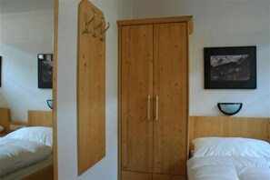 A bedroom with a wooden wardrobe, two beds, a wall-mounted shelf with a bowl, and a framed picture.