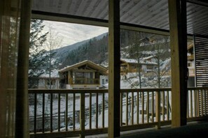 A wooden cabin with a balcony overlooking a snowy landscape and mountains.