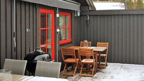 An outdoor patio with a barbecue grill, wooden tables and chairs, and a red-framed window. - 5 Person Holiday Home in Sarna (Sarna)