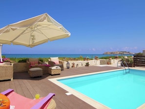 Ein Poolbereich mit Korbmöbeln, einem Pool und Blick auf das Meer.