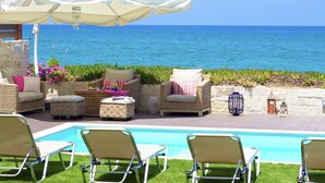 Un espace aménagé au bord de la piscine, avec des meubles en osier, un parasol blanc et une vue sur l’océan.