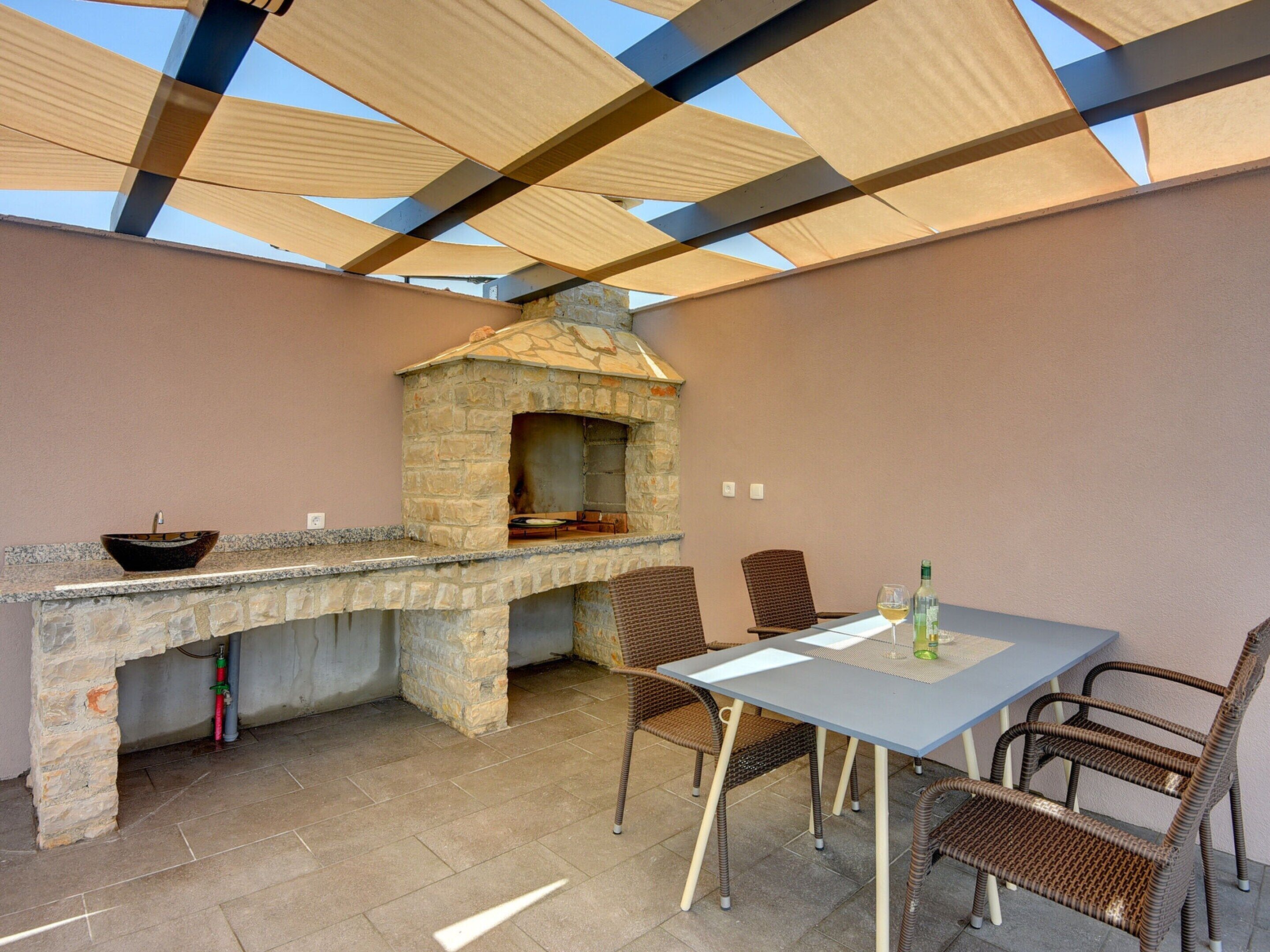Un área de cocina exterior con un horno de piedra, un fregadero y una mesa con sillas.