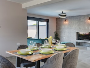 A dining area with a wooden table set for four, surrounded by cushioned chairs. A large window provides natural light, and a flat-screen TV is mounted on the wall. - Villa in Valbandon Near Fazana Beaches (Fazana)