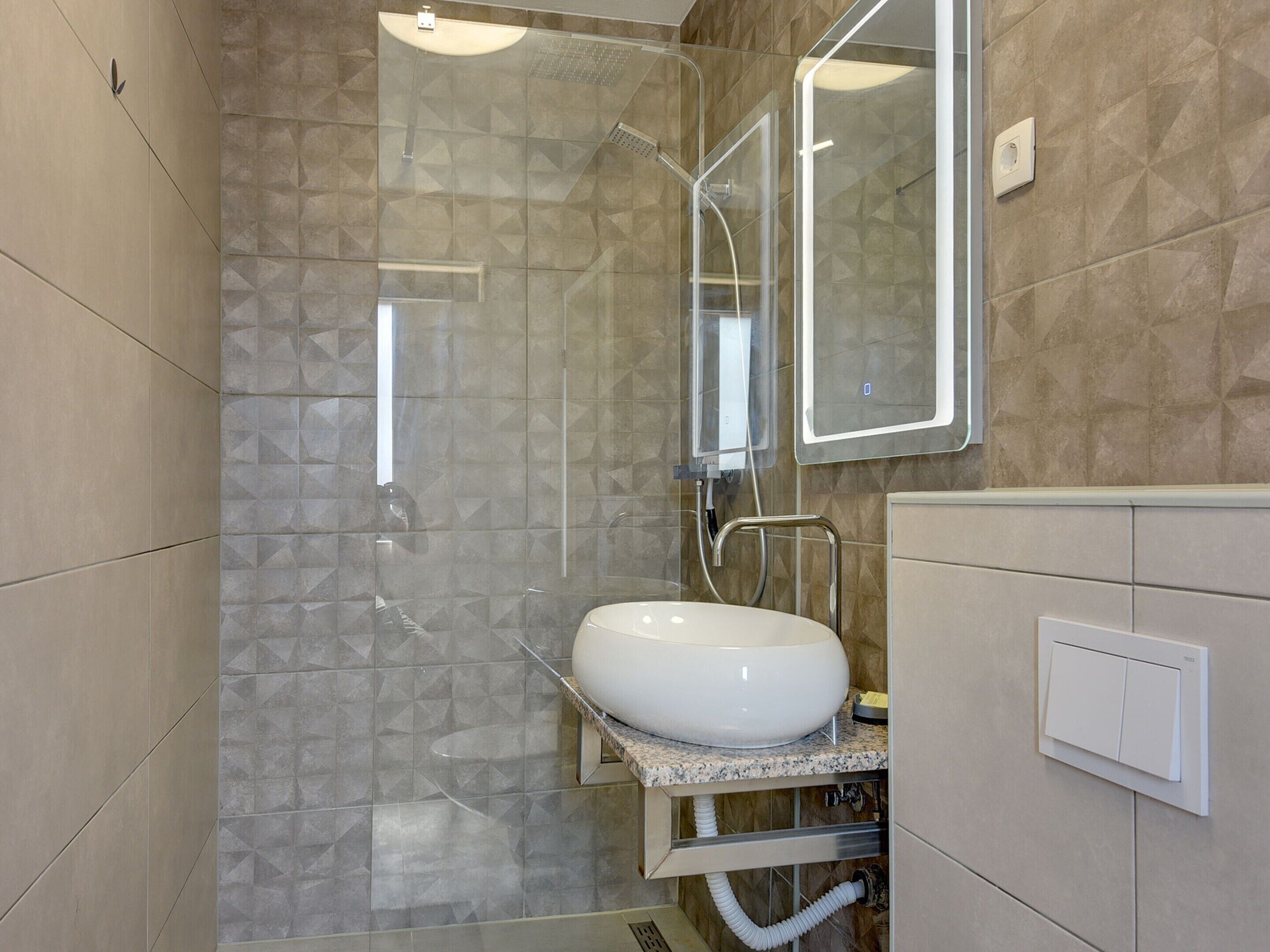 A modern bathroom with a glass-enclosed shower, a white sink, and a mirror.