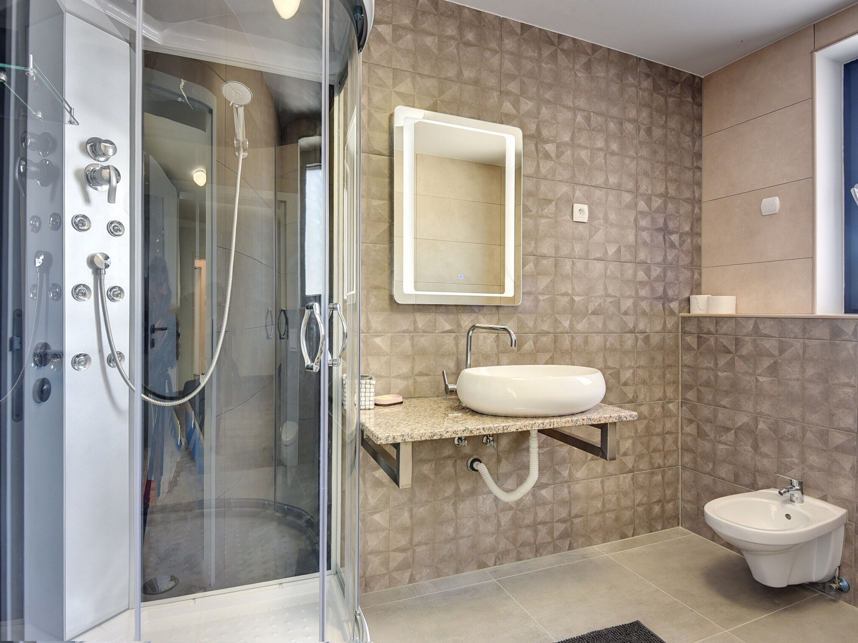 A modern bathroom with a glass-enclosed shower, a vanity with a sink, a bidet, and a mirror.