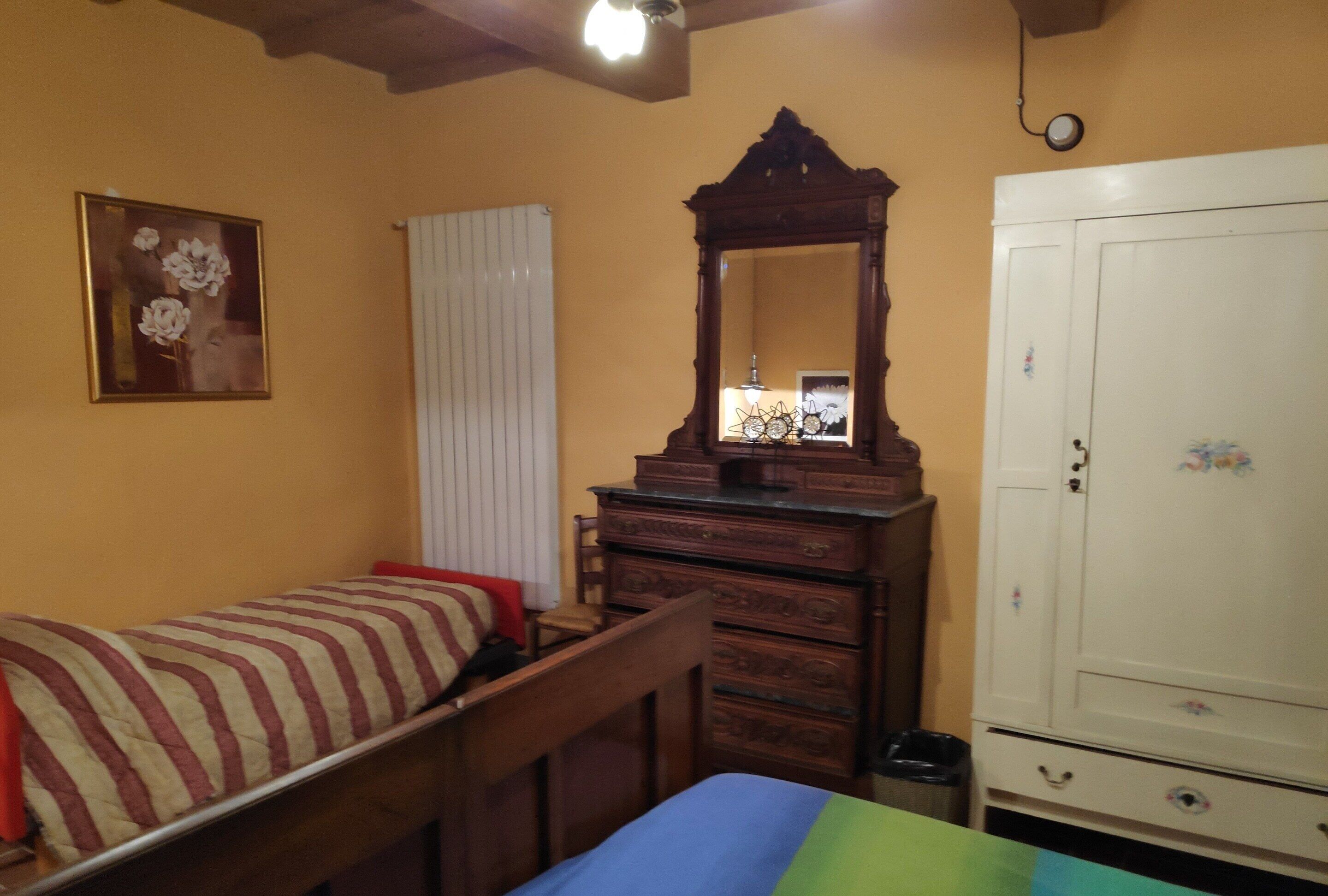 A bedroom with a bed, a dresser, a mirror, a wardrobe, and a radiator.