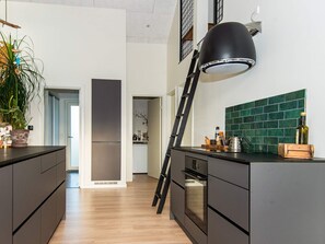 A modern kitchen with dark cabinetry, a black pendant light, a green tiled backsplash, and a wooden ladder leaning against the counter. - Holiday Home in Tarm (Tarm)