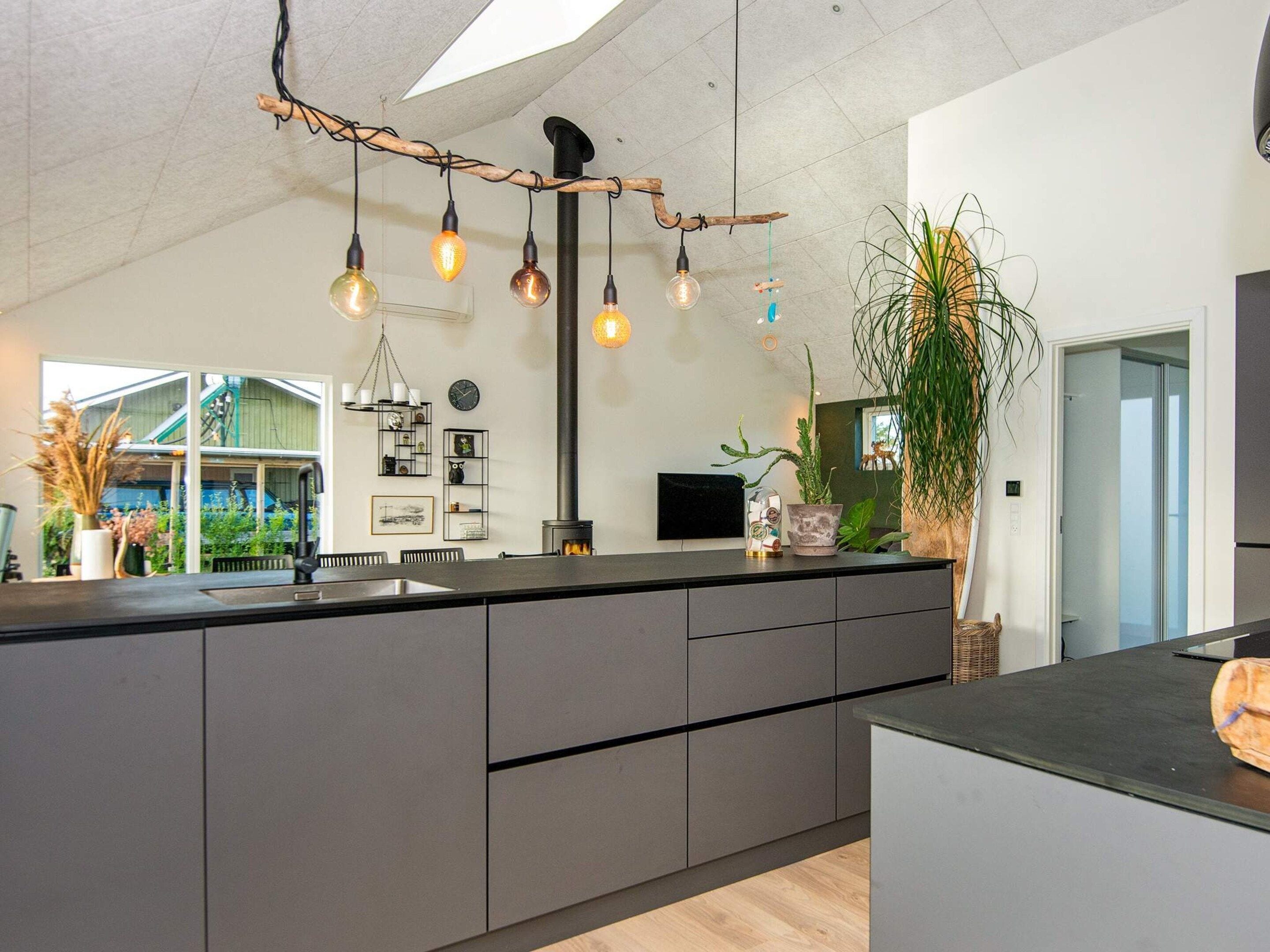 A modern kitchen with a large island, pendant lighting, and a view of a green house.