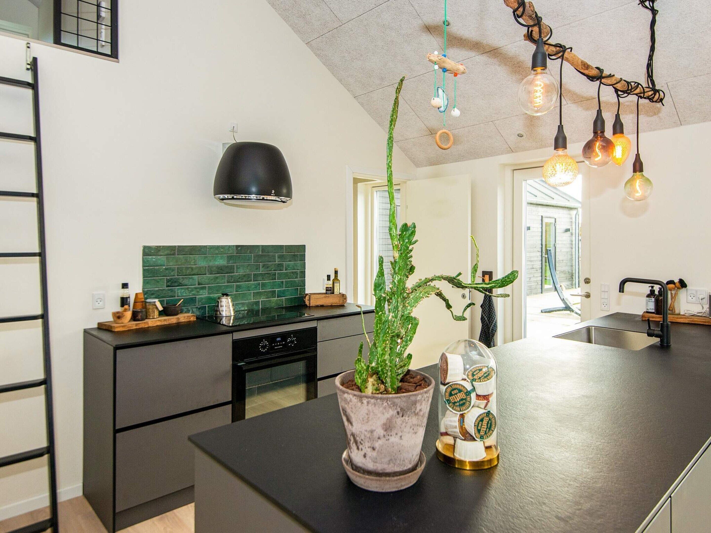 Una cocina moderna con encimera negra, salpicadero verde y lámpara colgante.