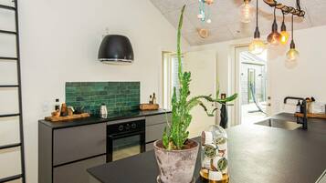 Una cocina moderna con encimera negra, salpicadero verde y lámpara colgante.