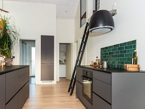 A modern kitchen with dark cabinetry, a black pendant light, and a green tiled backsplash. - Holiday Home in Tarm (Tarm)