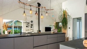 Une cuisine moderne dotée d’un îlot central, d’un éclairage suspendu et offrant une vue sur une serre.