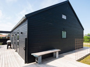 A black wooden building with a sloped roof, a bench, and a small window. - Holiday Home in Tarm (Tarm)