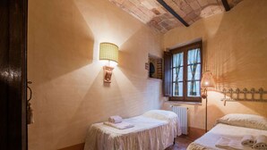 A cozy room with two single beds, a window with curtains, a wall-mounted lamp, and a radiator.