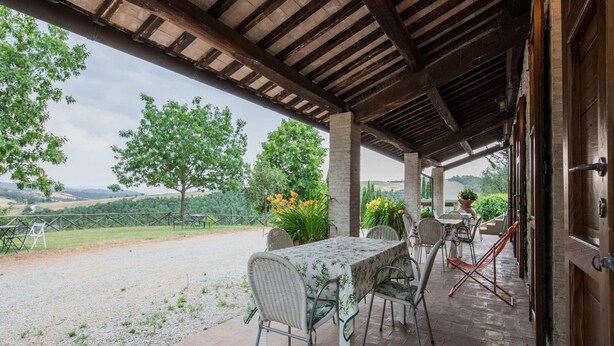 An outdoor patio with a table and chairs, a covered area with a wooden ceiling, and a view of the countryside.