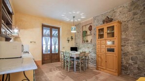 A cozy kitchen with a dining table, chairs, a wooden cabinet, and a stone wall.