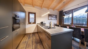 Een moderne keuken met houten balkenplafond, een groot eiland met een spoelbak en uitzicht op bergen door grote ramen.