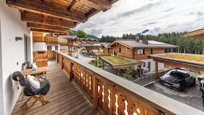 Een houten balkon met uitzicht op een dorp, een auto en een berg op de achtergrond.