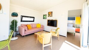 A modern living room with a pink sofa, yellow armchairs, a flat-screen TV, and a potted plant. - Wheelchair-friendly Retreat (Callantsoog)