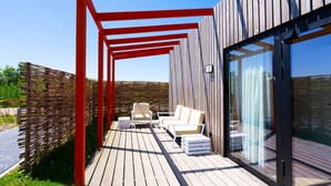 A wooden deck with outdoor seating and a glass door leading to a modern building. - Wheelchair-friendly Retreat (Callantsoog)