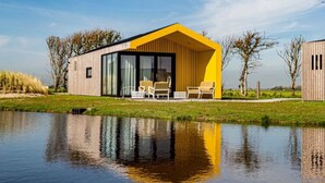 A modern house with a yellow facade, large windows, and a patio with outdoor furniture. - Wheelchair-friendly Retreat (Callantsoog)