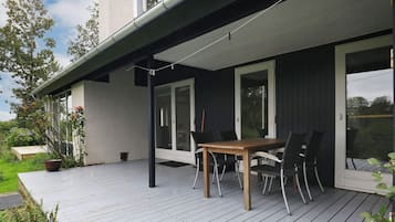 A wooden deck with a table and chairs, a potted plant, and a view of the surrounding greenery.