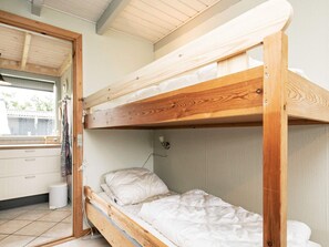 A bunk bed with a wooden frame, a white mattress, and a headboard. There is a window with curtains, a white sink, and a small trash bin. - 6 Person Holiday Home in Roslev (Roslev)