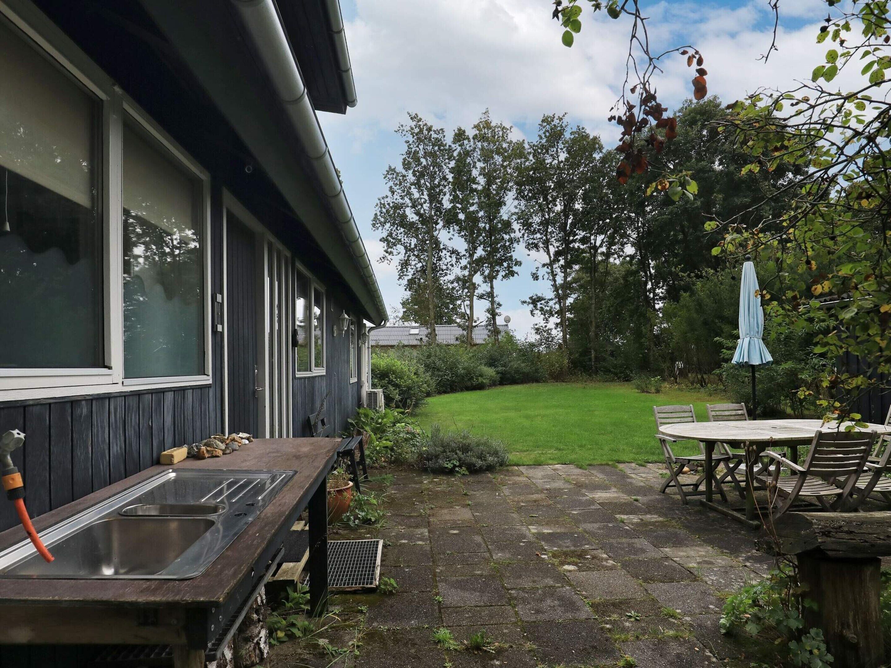 Eine Terrasse mit Tisch, Stühlen, einem Grill und einem Spülbecken.