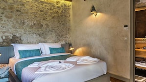 A bedroom with a stone wall, a wooden ceiling, a bed with white and teal bedding, and a nightstand with a lamp.