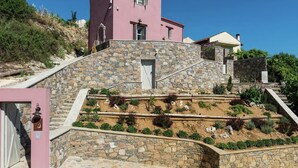 A pink building with a stone staircase leading to a door, surrounded by a landscaped garden.
