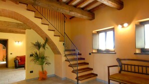 A spacious interior with a wooden staircase, a large potted plant, a bench, and a window with curtains. - Holiday Home in Urbania With Hill Views (Urbania)