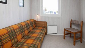 A room with a plaid sofa, a wooden chair, a radiator, and a window with a view of houses. - 6 Person Holiday Home in Lokken (Lokken)