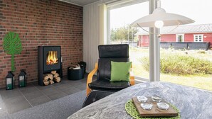 A cozy room with a brick wall, a fireplace, a comfortable chair, and a table with candle holders. - 6 Person Holiday Home in Lokken (Lokken)