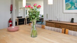 A dining area with a wooden table, a vase with pink roses, and a painting on the wall. - 6 Person Holiday Home in Lokken (Lokken)
