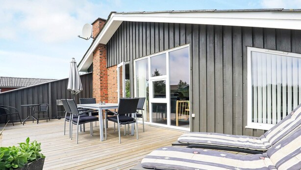 A deck with a table and chairs, a lounge chair, and a potted plant. - 6 Person Holiday Home in Lokken (Lokken)