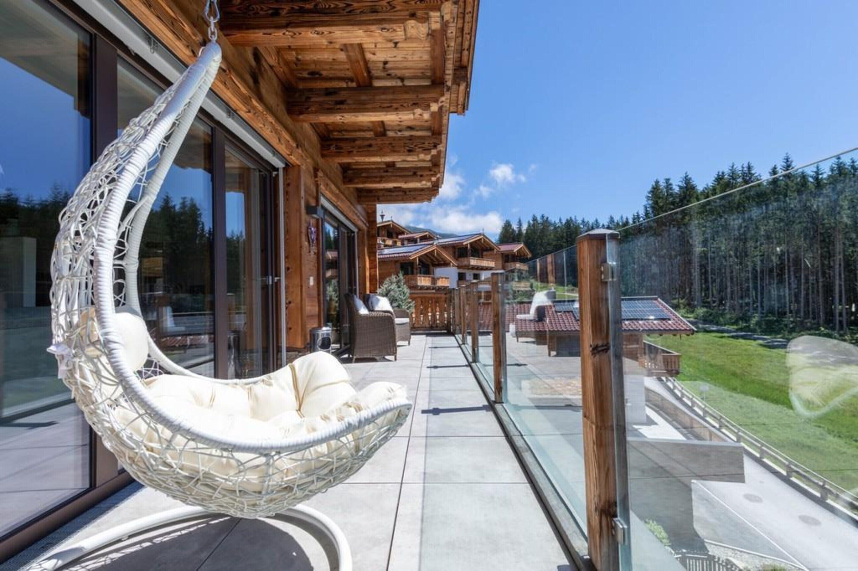 A balcony with a hanging chair, wooden railings, and a view of a mountainous landscape.